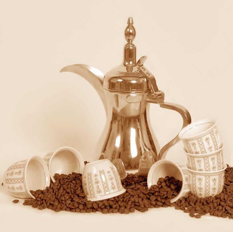A brass dallah coffee pot with small handleless cups and coffee beans