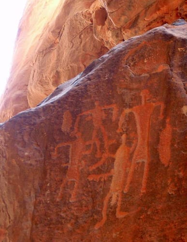 Ancient rock carvings of human figures on a red sandstone wall in Khazali Canyon