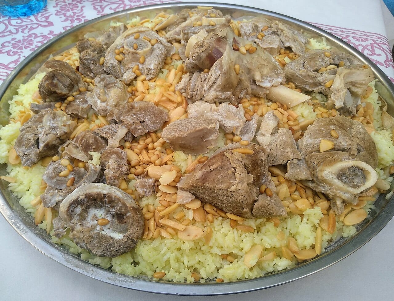 A large platter of mansaf with lamb pieces on yellow rice topped with toasted nuts