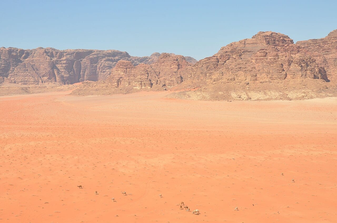 View from the top of a red sand dune across the Wadi Rum valley to sandstone cliffs