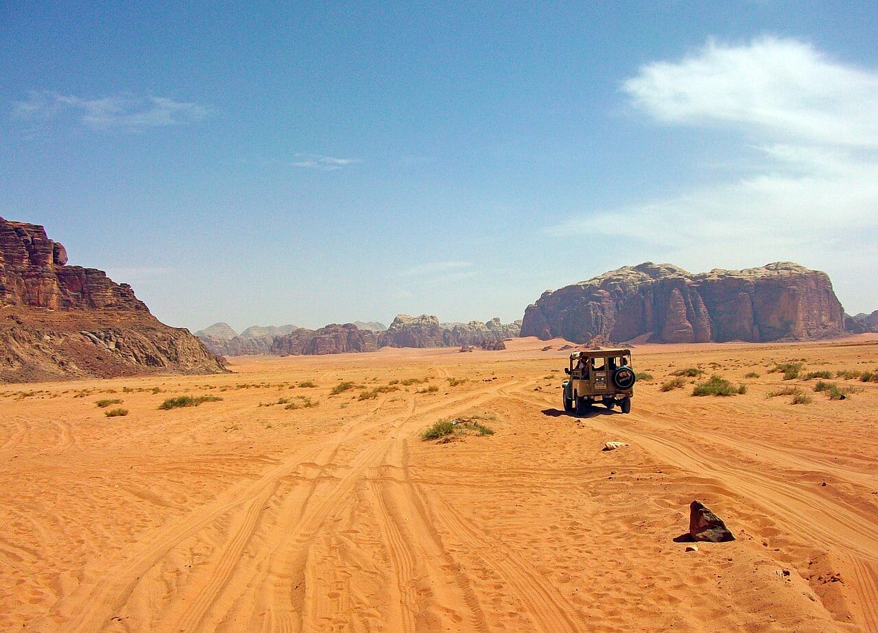 A four-wheel-drive jeep driving into the sand of Wadi Rum