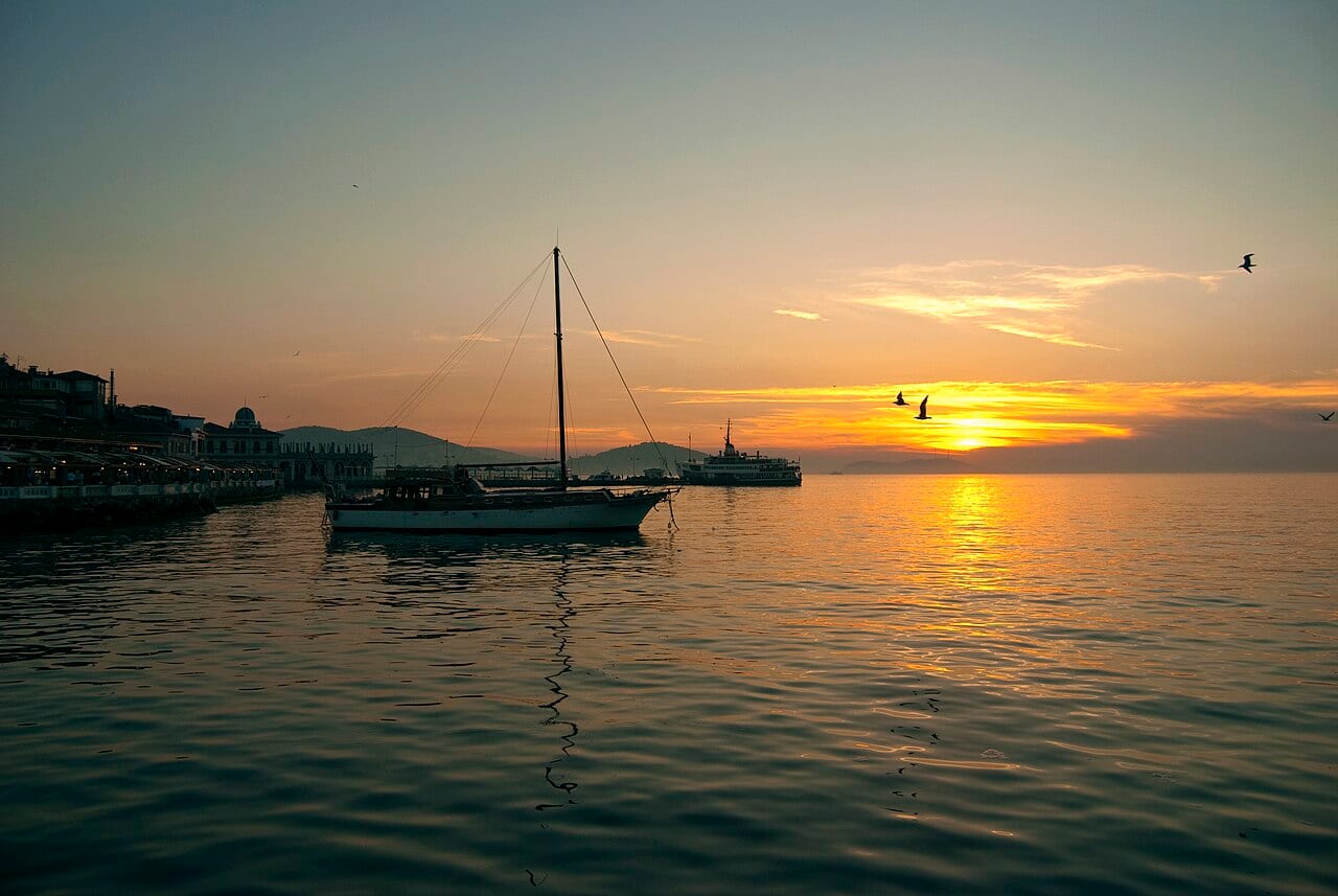 Sunset over the harbour of Büyükada with a sailing boat on calm water