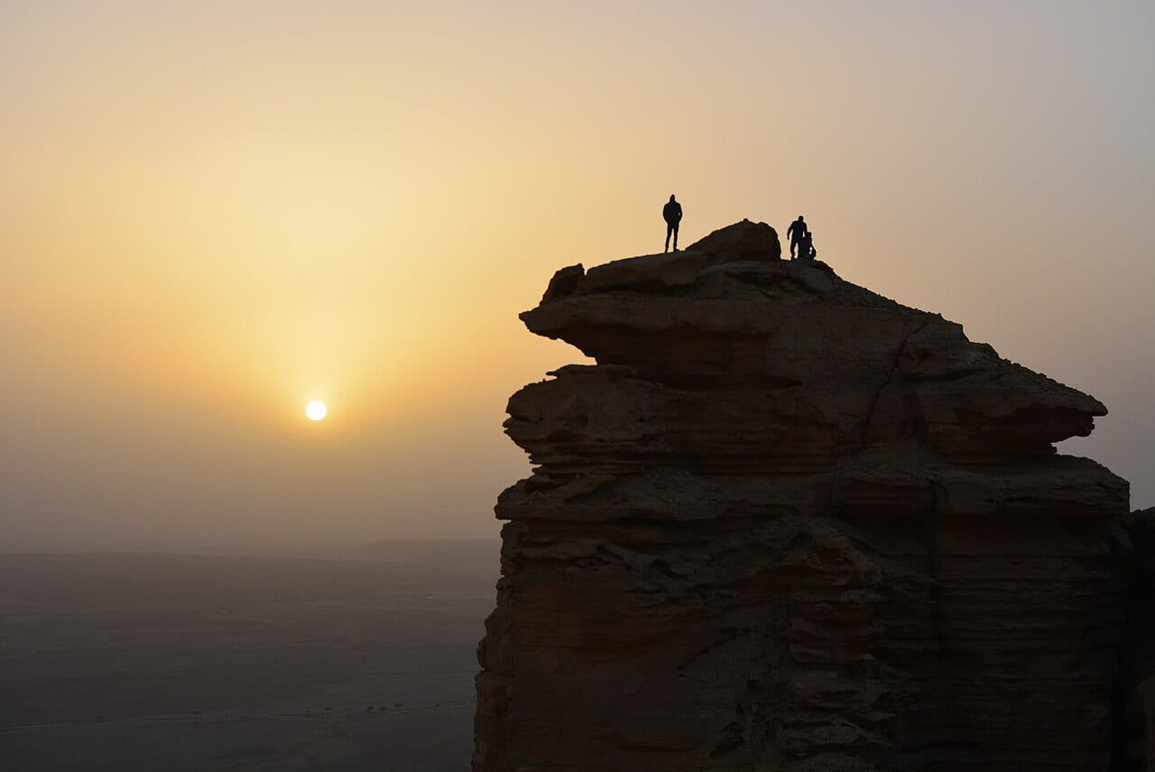 A person standing on a cliff at the Edge of the World near Riyadh at sunset