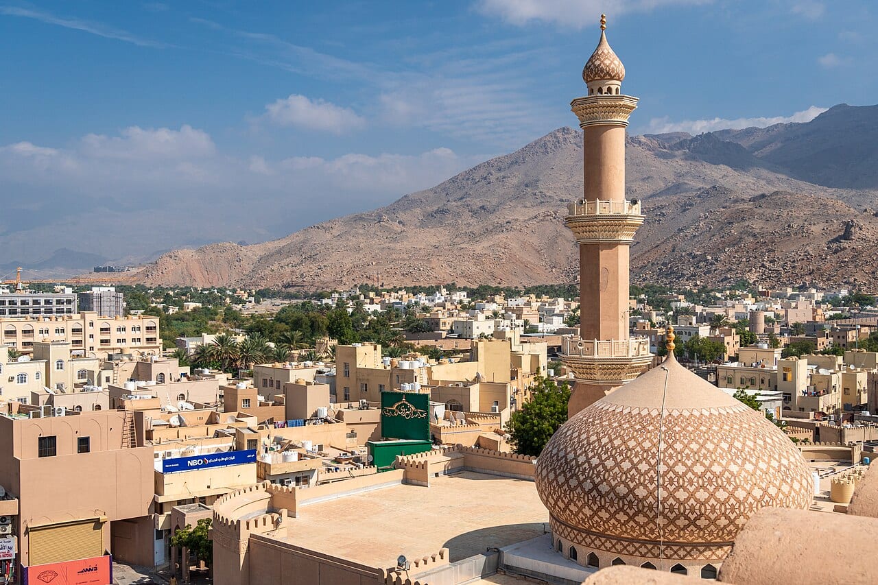 برج قلعة نزوى الدائري مع قبة مسجد وجبال خلفه